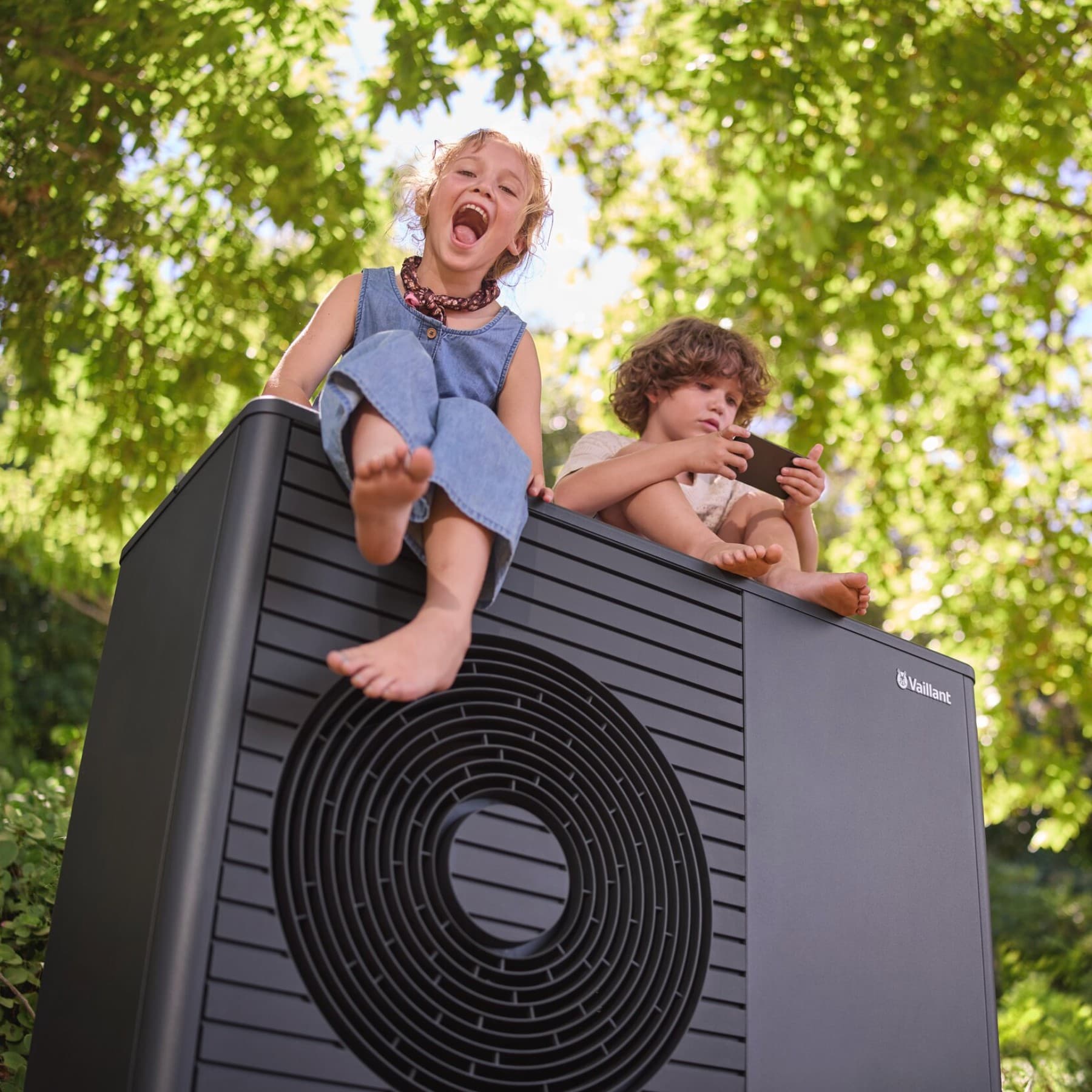 Két gyermek ül egy Vaillant aroTHERM plus hőszivattyún
