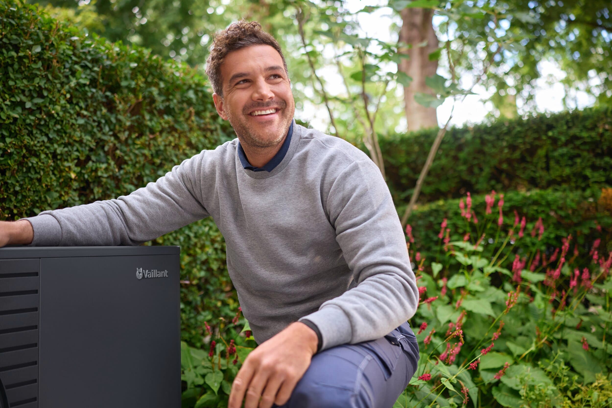 Egy férfi térdel az aroTHERM pro mellett a kertben